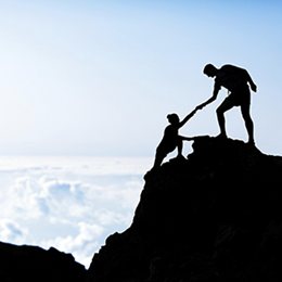 photo of person at the top of a mountain peak pulling another person up